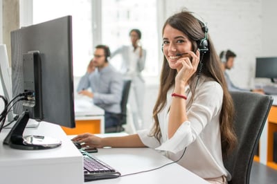 A virtual receptionist sitting at her desk speaks on the phone using a headset