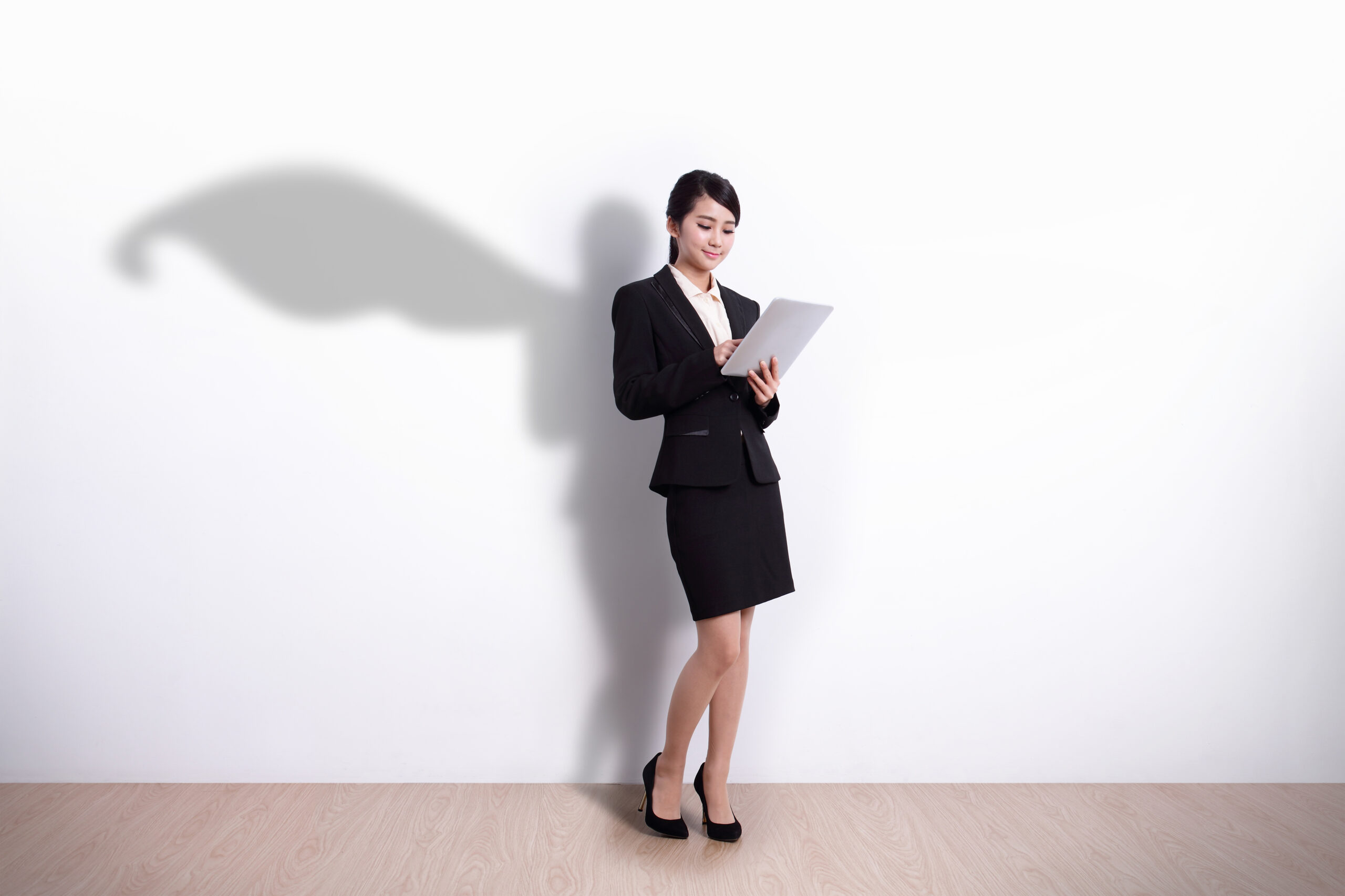 Superhero Business Woman using digital tablet pc computer with white wall background, great for your design or text, asian