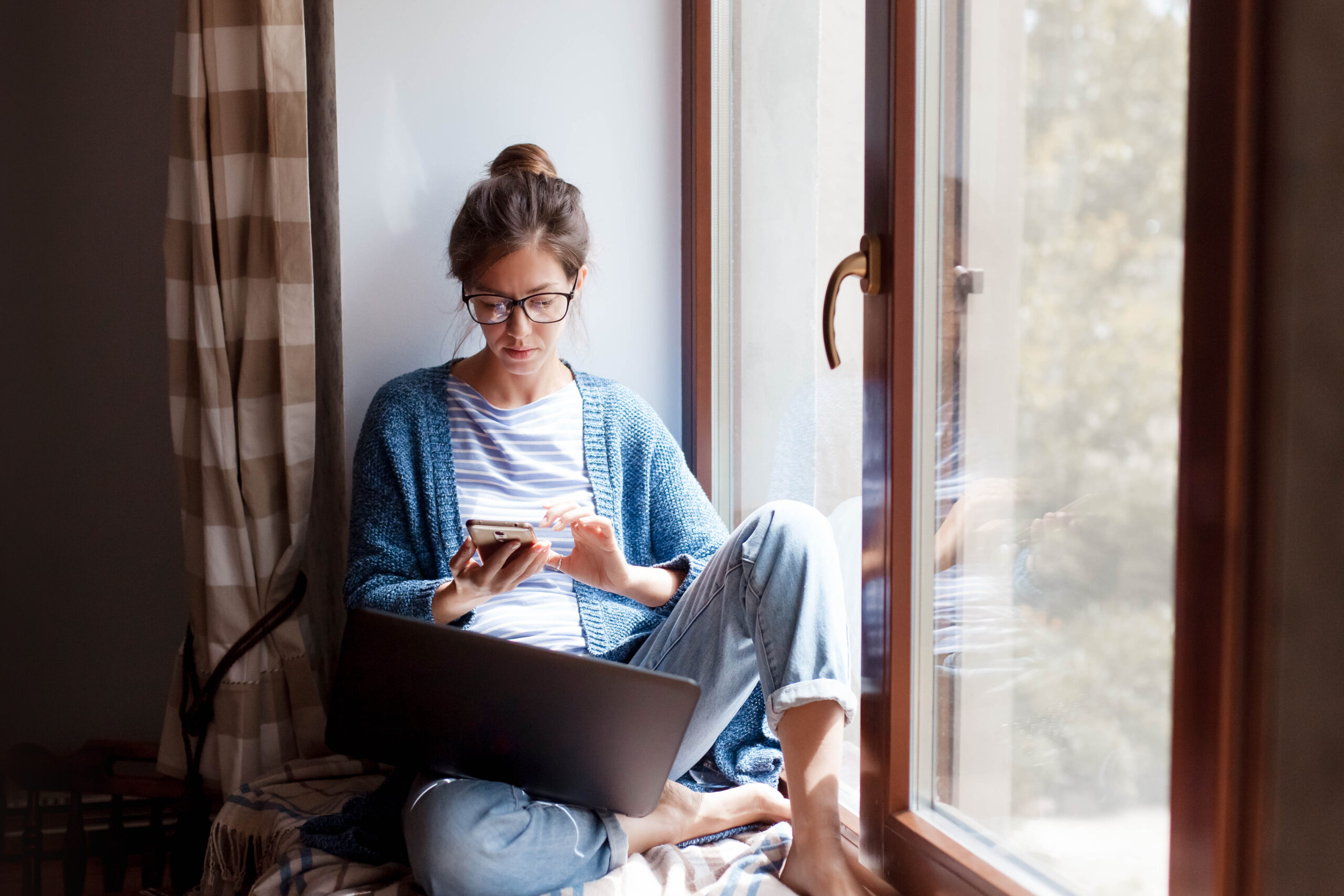 Young woman working from home office. Freelancer using laptop, phone and the Internet. Young woman working from home office. Freelancer using laptop, phone and the Internet. Workplace in living room on windowsill. Concept of female business, career, shopping online. Lifestyle moment.
