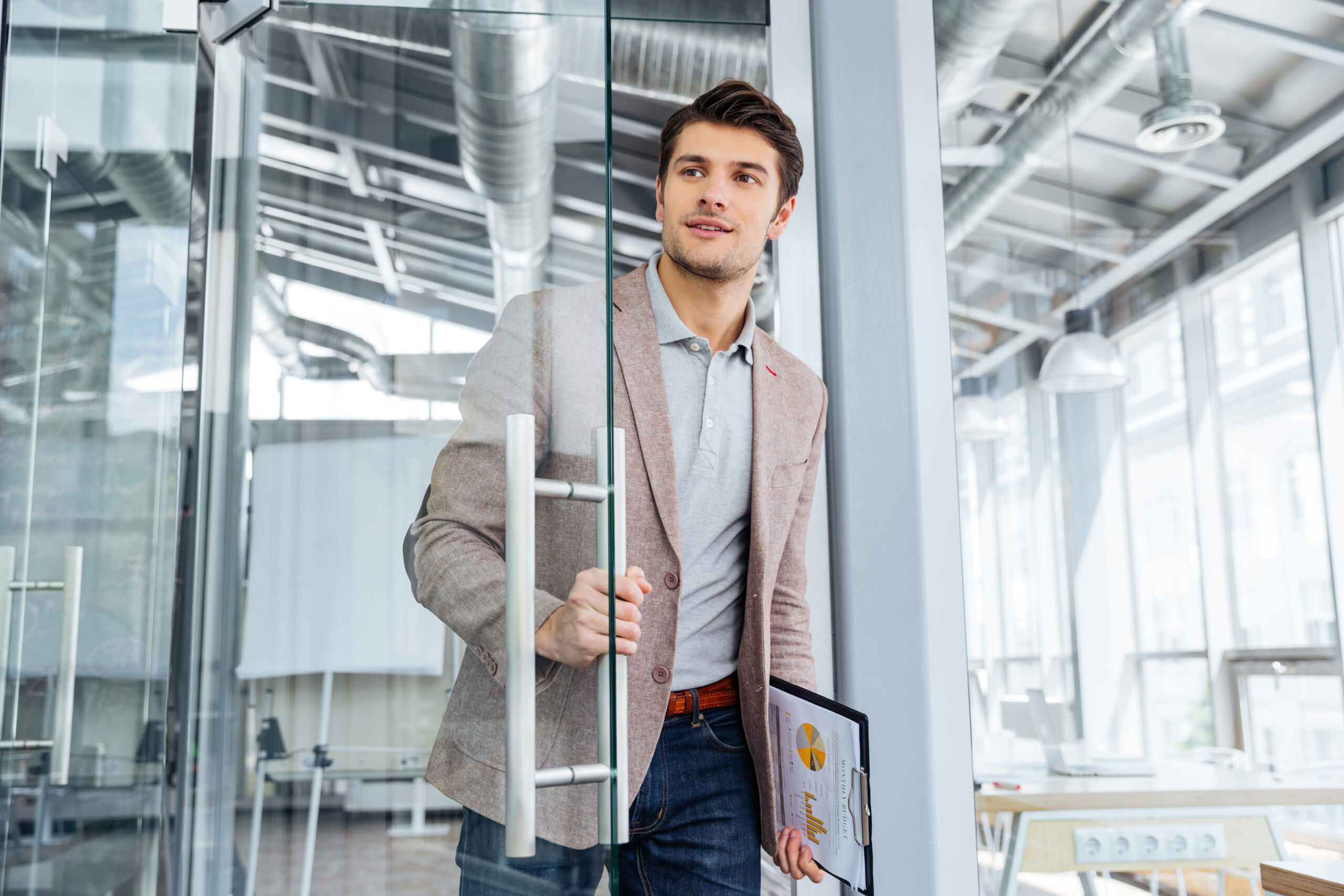 Handsome young businessman with clipboard entering the door in office